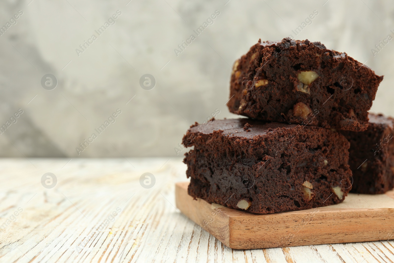 Photo of Delicious brownies with nuts on white wooden table, closeup. Space for text