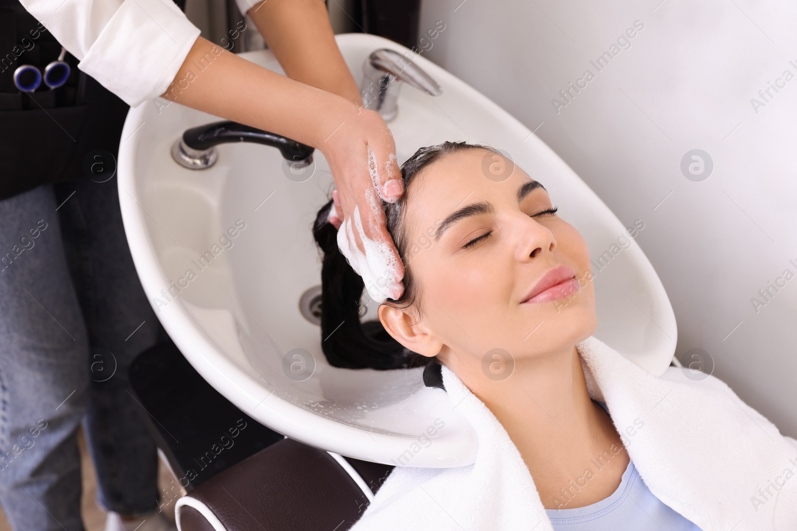 Photo of Professional hairdresser washing woman's hair in beauty salon, closeup