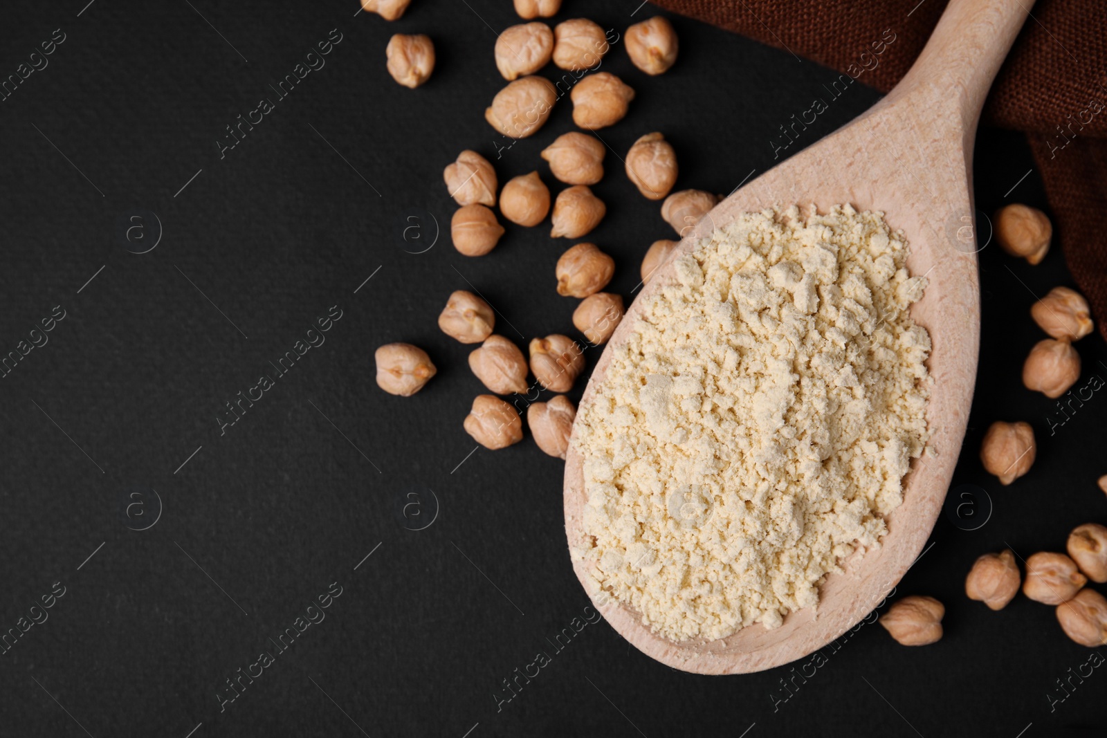 Photo of Spoon with chickpea flour and seeds on black table, top view. Space for text