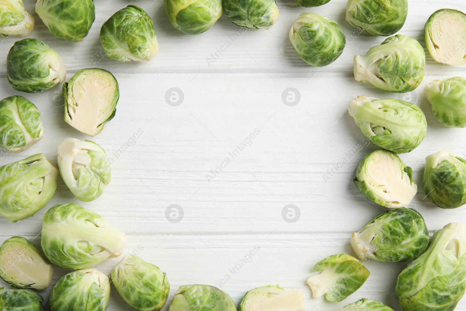 Photo of Frame made with fresh Brussels sprouts on white wooden table, flat lay. Space for text