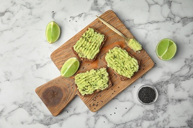 Photo of Tasty crisp rye toasts with avocado on wooden board, top view