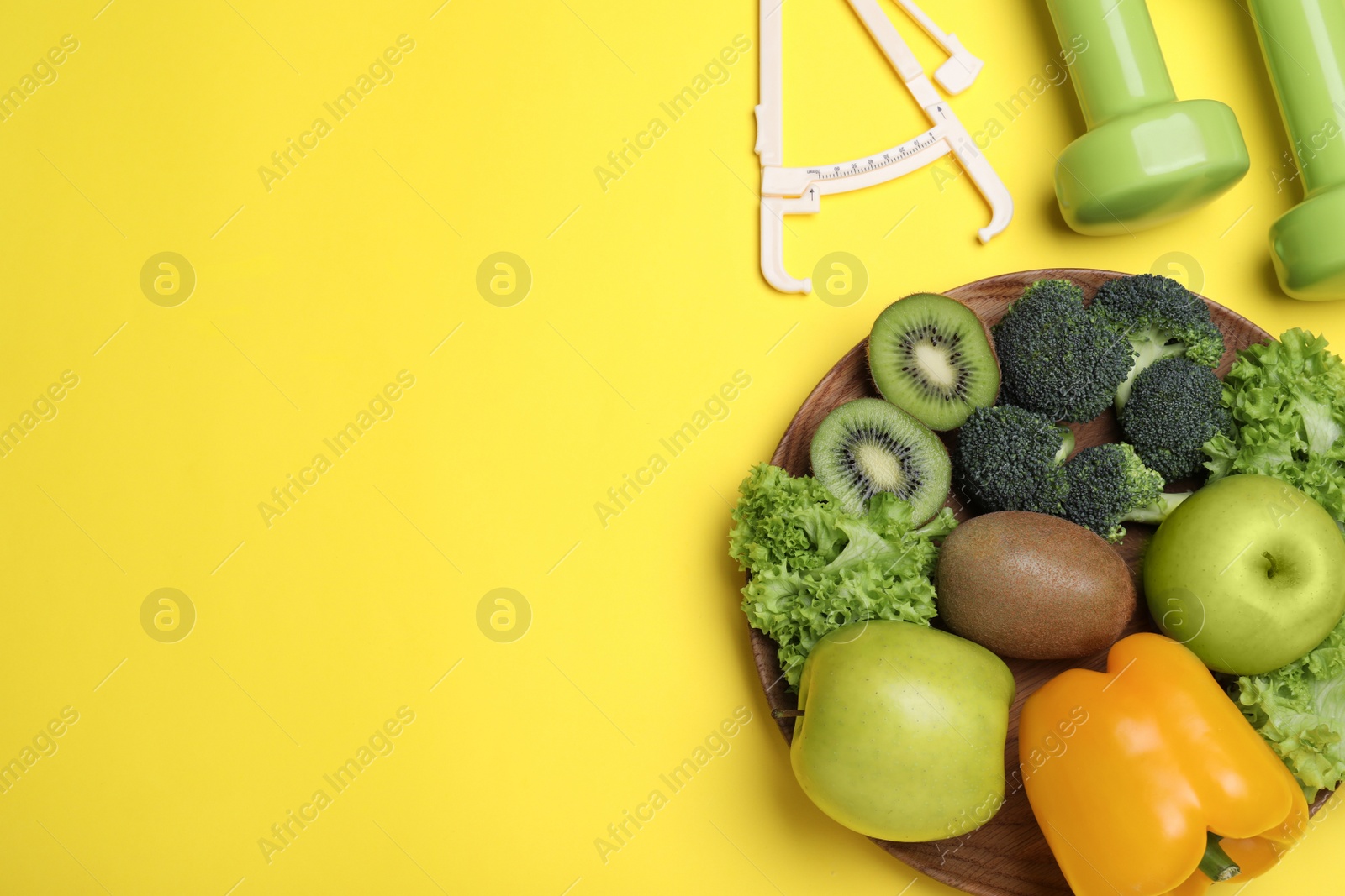 Photo of Fruits, vegetables, dumbbells and caliper on yellow background, flat lay with space for text. Visiting nutritionist