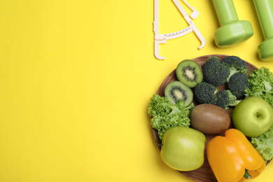 Fruits, vegetables, dumbbells and caliper on yellow background, flat lay with space for text. Visiting nutritionist