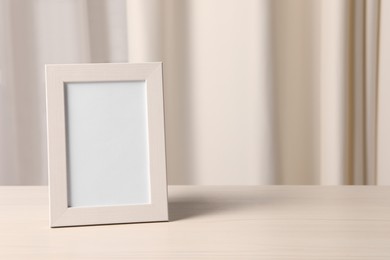 Photo of Empty square frame on white wooden table indoors, space for text
