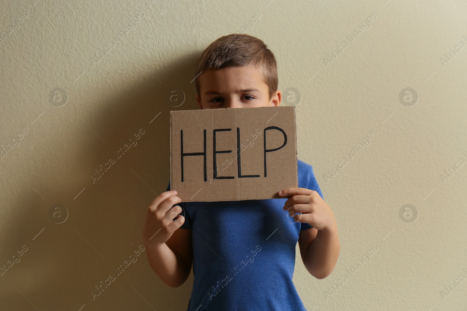 Photo of Little boy with sign HELP on yellow background. Child in danger