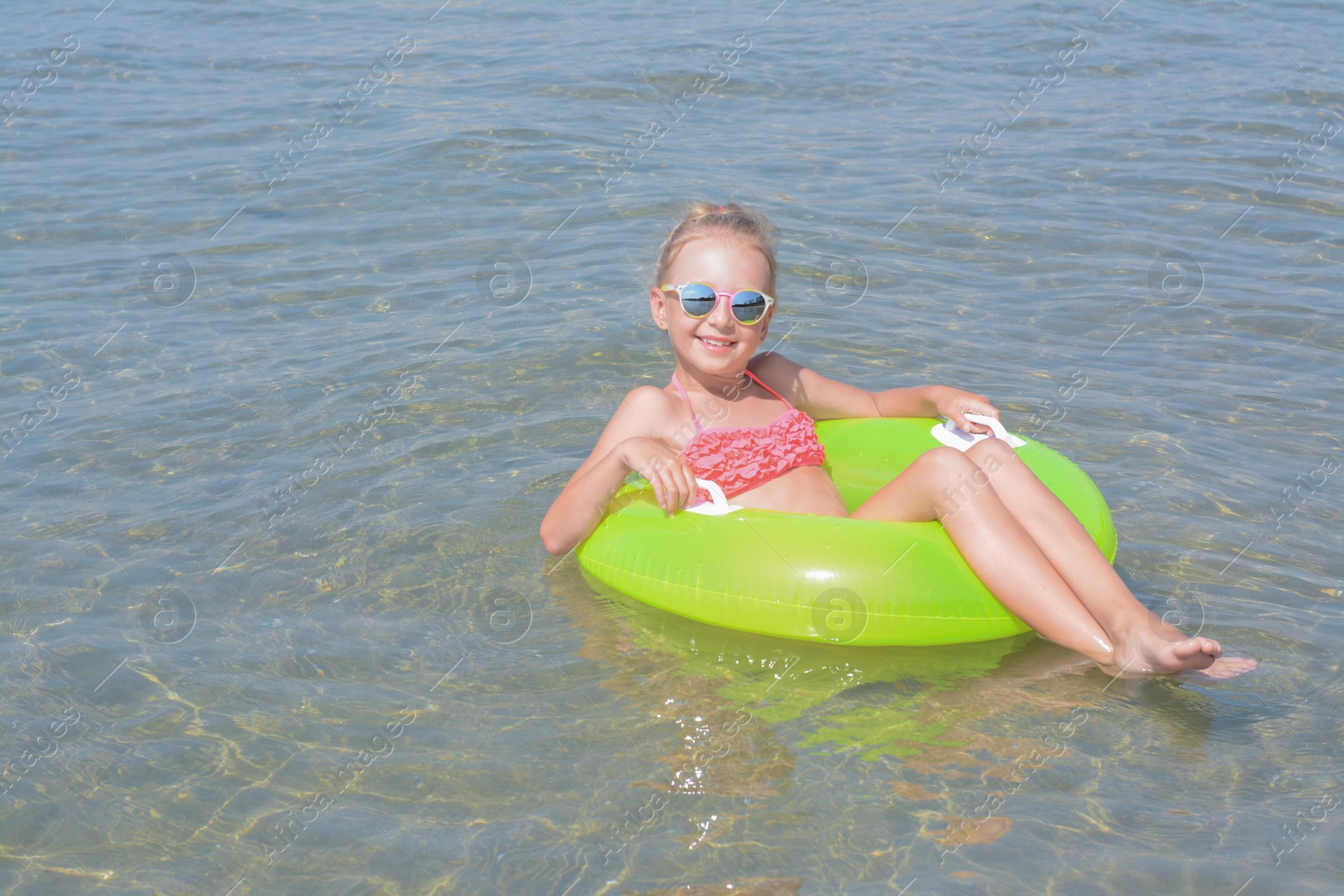 Photo of Happy little girl with inflatable ring in sea on sunny day, space for text