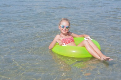 Photo of Happy little girl with inflatable ring in sea on sunny day, space for text