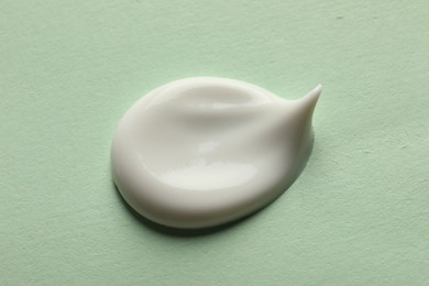 Sample of face cream on light green background, top view