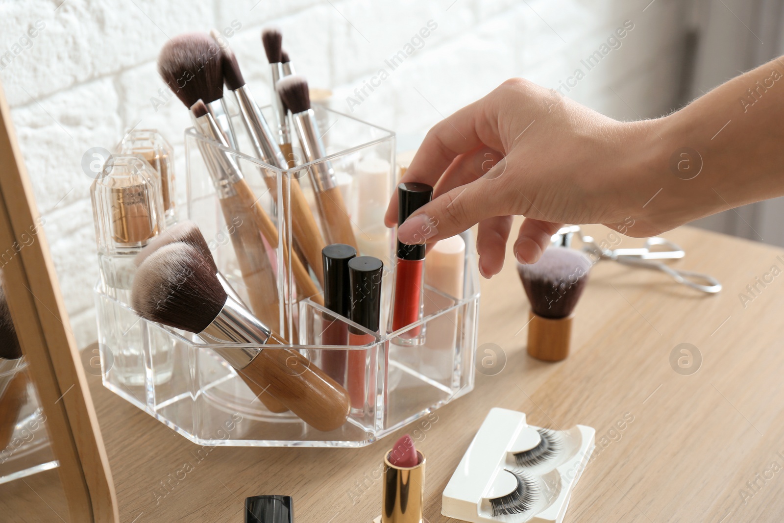 Photo of Woman taking cosmetics from organizer for makeup products on table