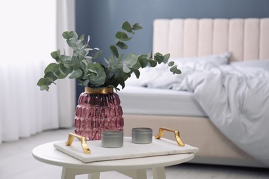 Photo of Candles and eucalyptus branches on white table in bedroom. Interior element
