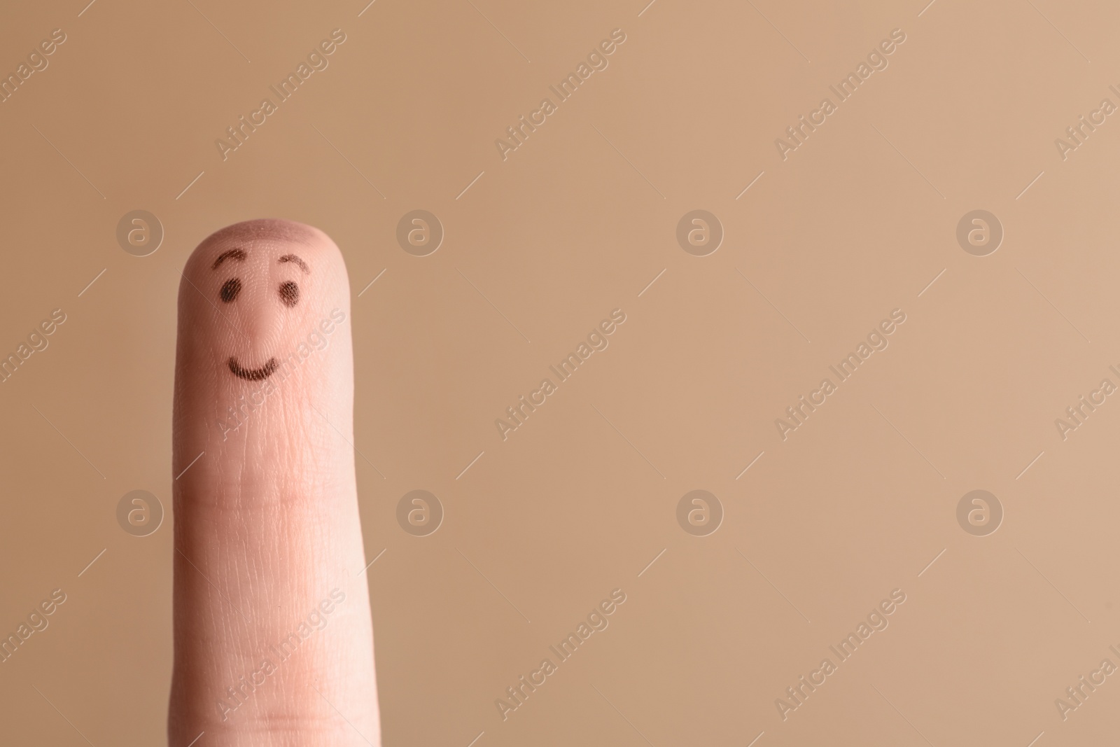 Photo of Finger with drawing of happy face on brown background. Space for text