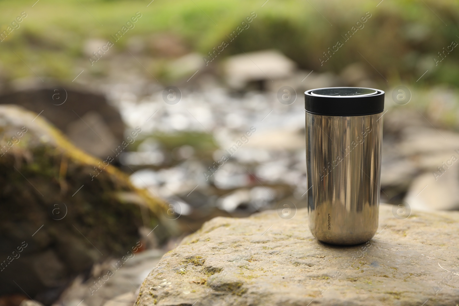 Photo of Metallic thermo tumbler on stone outdoors, space for text