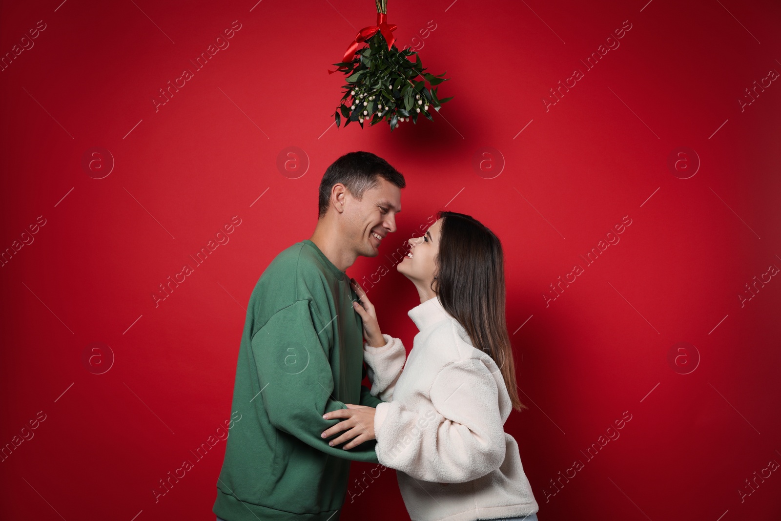 Photo of Happy couple standing under mistletoe bunch on red background