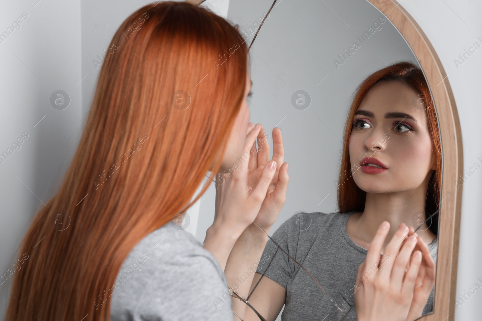 Photo of Sad young woman suffering from mental problems near broken mirror indoors