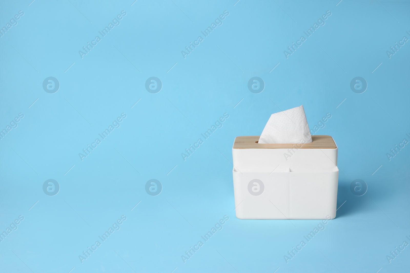 Photo of Holder with paper tissues on light blue background. Space for text