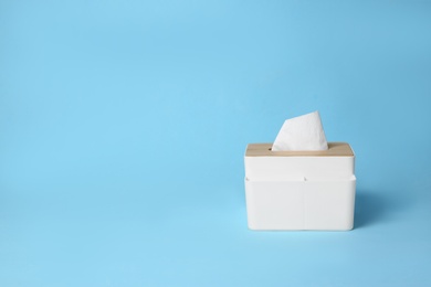 Photo of Holder with paper tissues on light blue background. Space for text