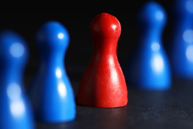 Photo of Choice concept. Red pawn among blue ones on black table, closeup