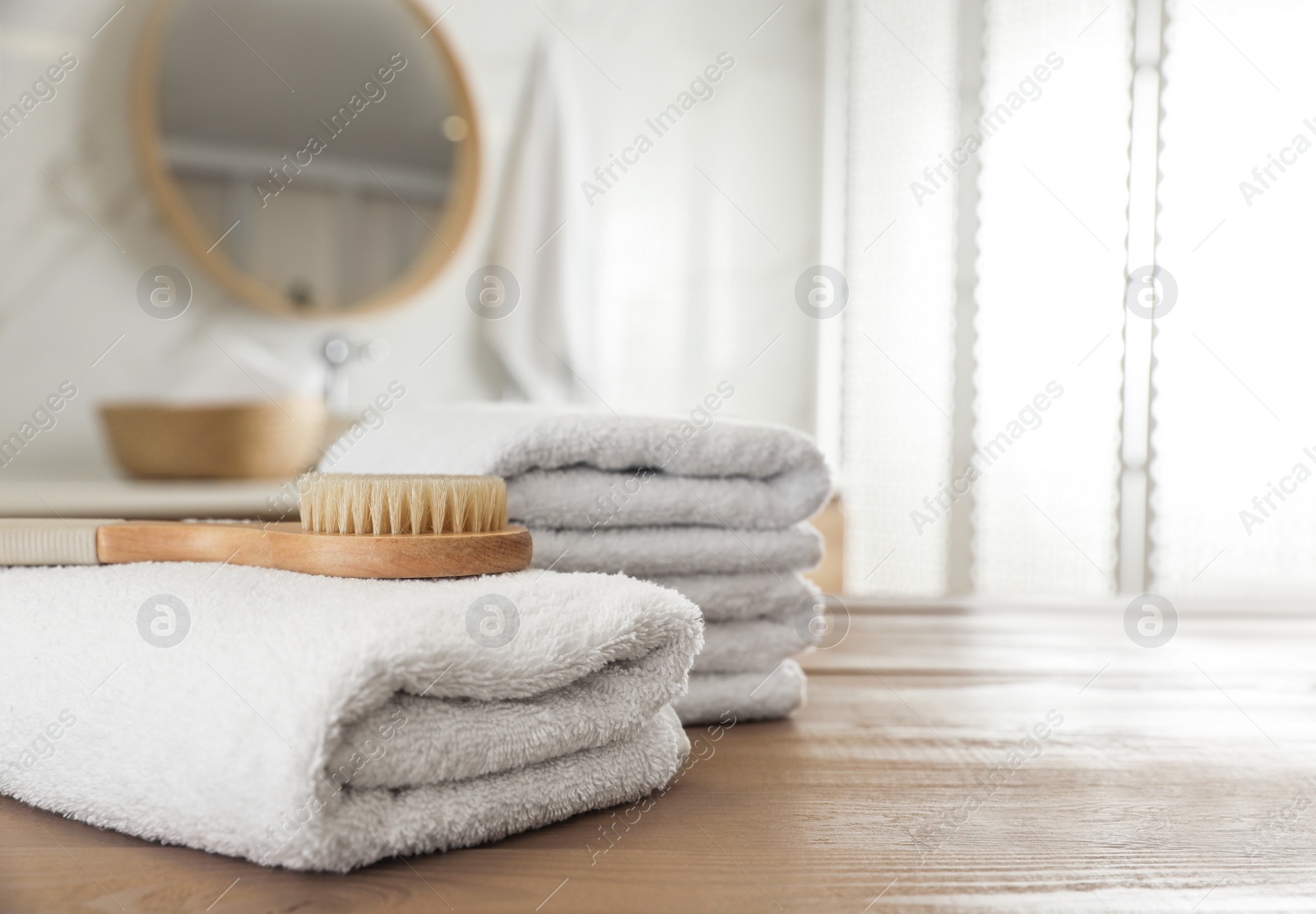 Photo of Stack of clean towels and massage brush on wooden table in bathroom. Space for text