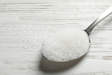 Spoon of sugar on white wooden table, closeup