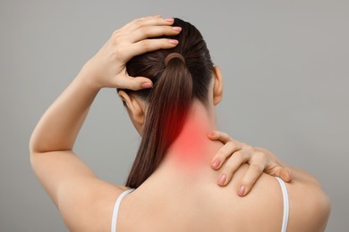 Woman suffering from neck pain on grey background, back view