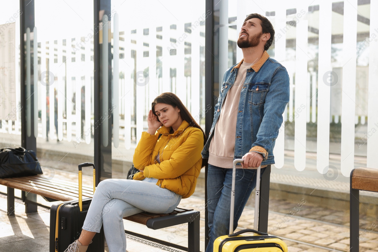 Photo of Being late. Worried couple with suitcases waiting at tram station outdoors