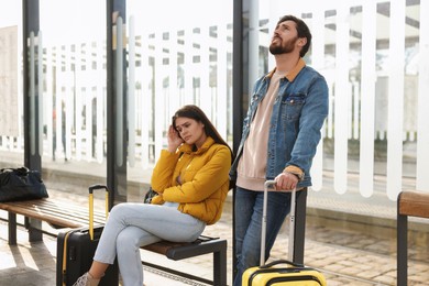 Being late. Worried couple with suitcases waiting at tram station outdoors
