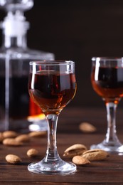Liqueur glasses with tasty amaretto and almonds on wooden table, closeup