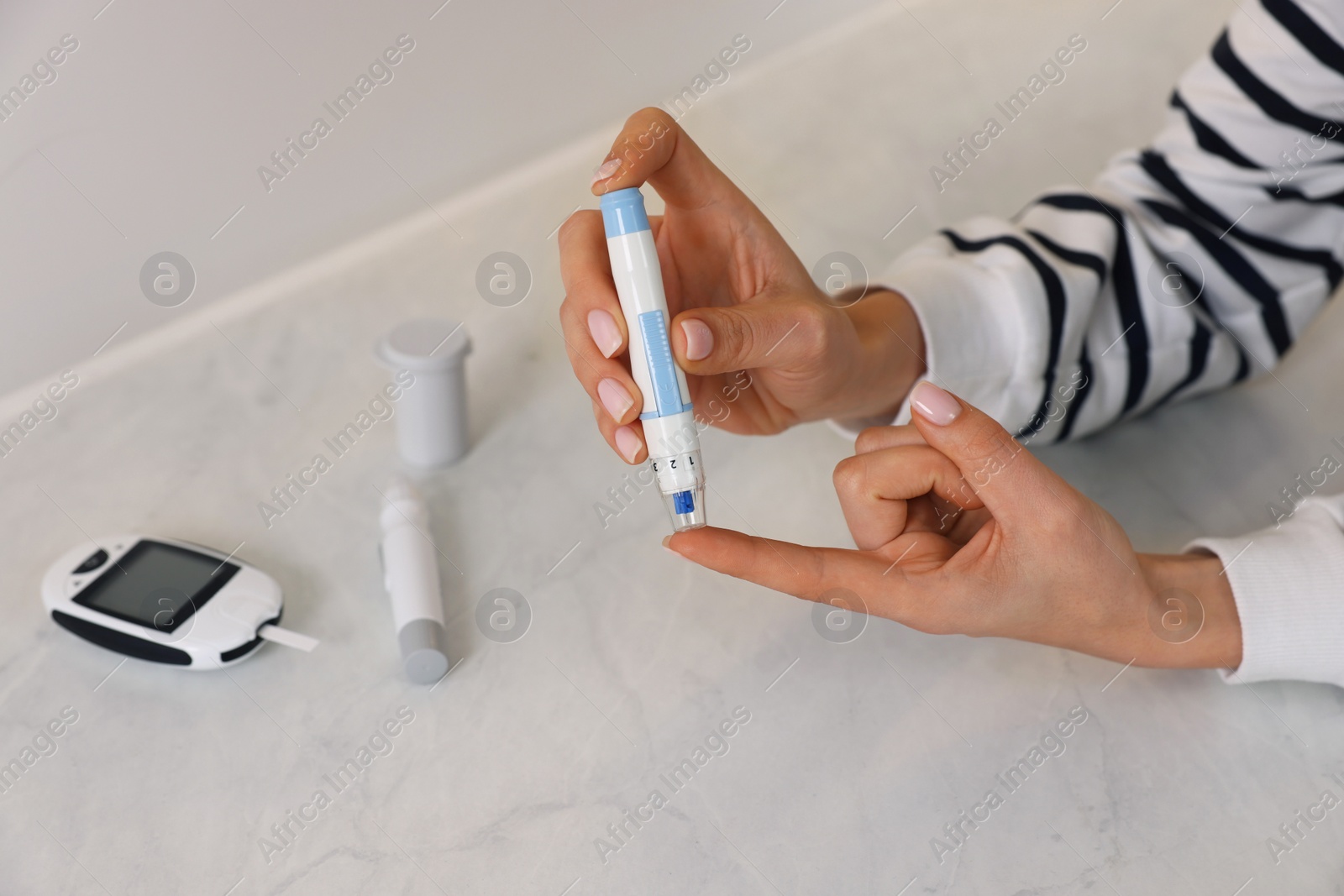 Photo of Diabetes. Woman using lancet pen at light table, closeup