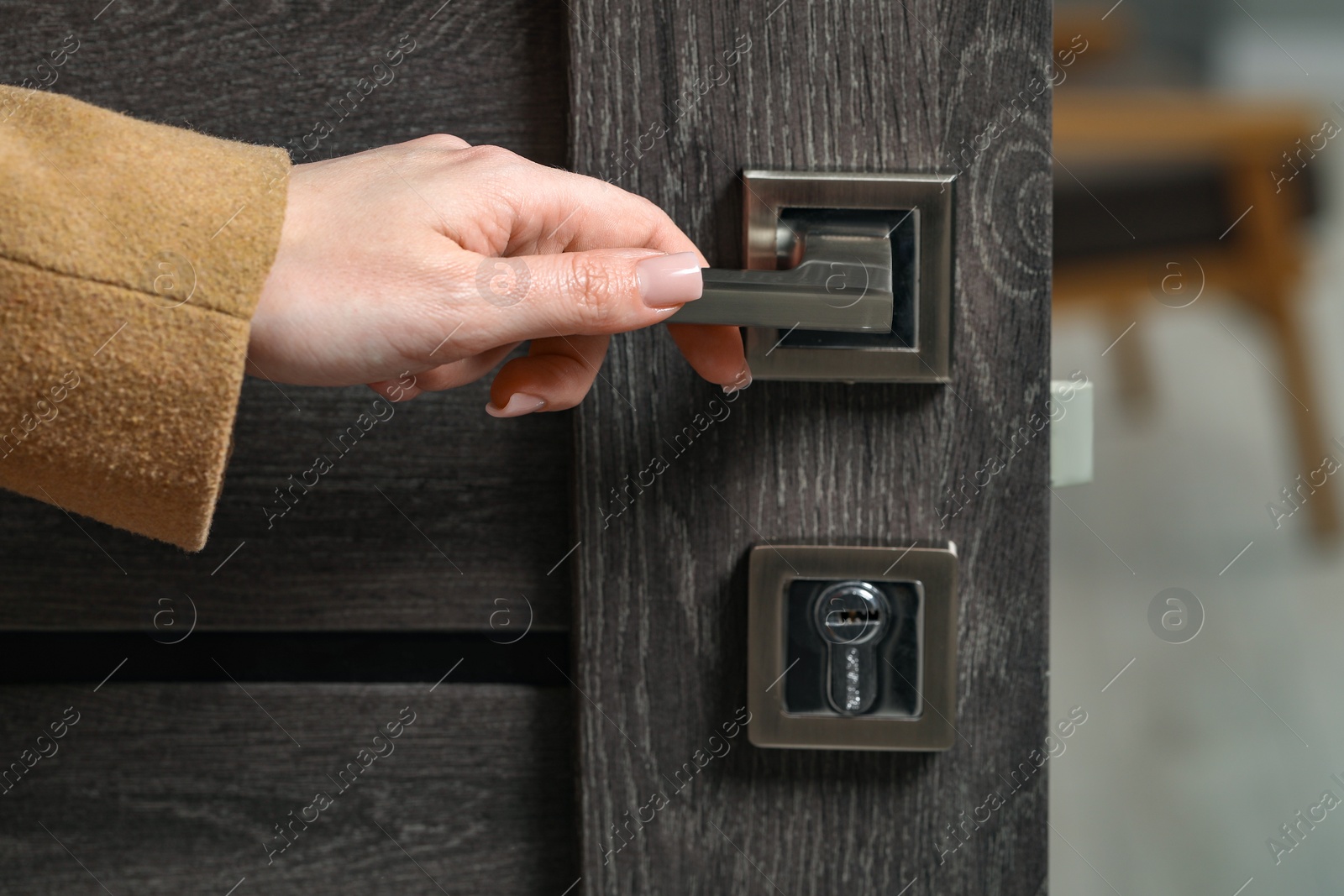 Photo of Woman opening wooden door indoors, closeup of hand on handle