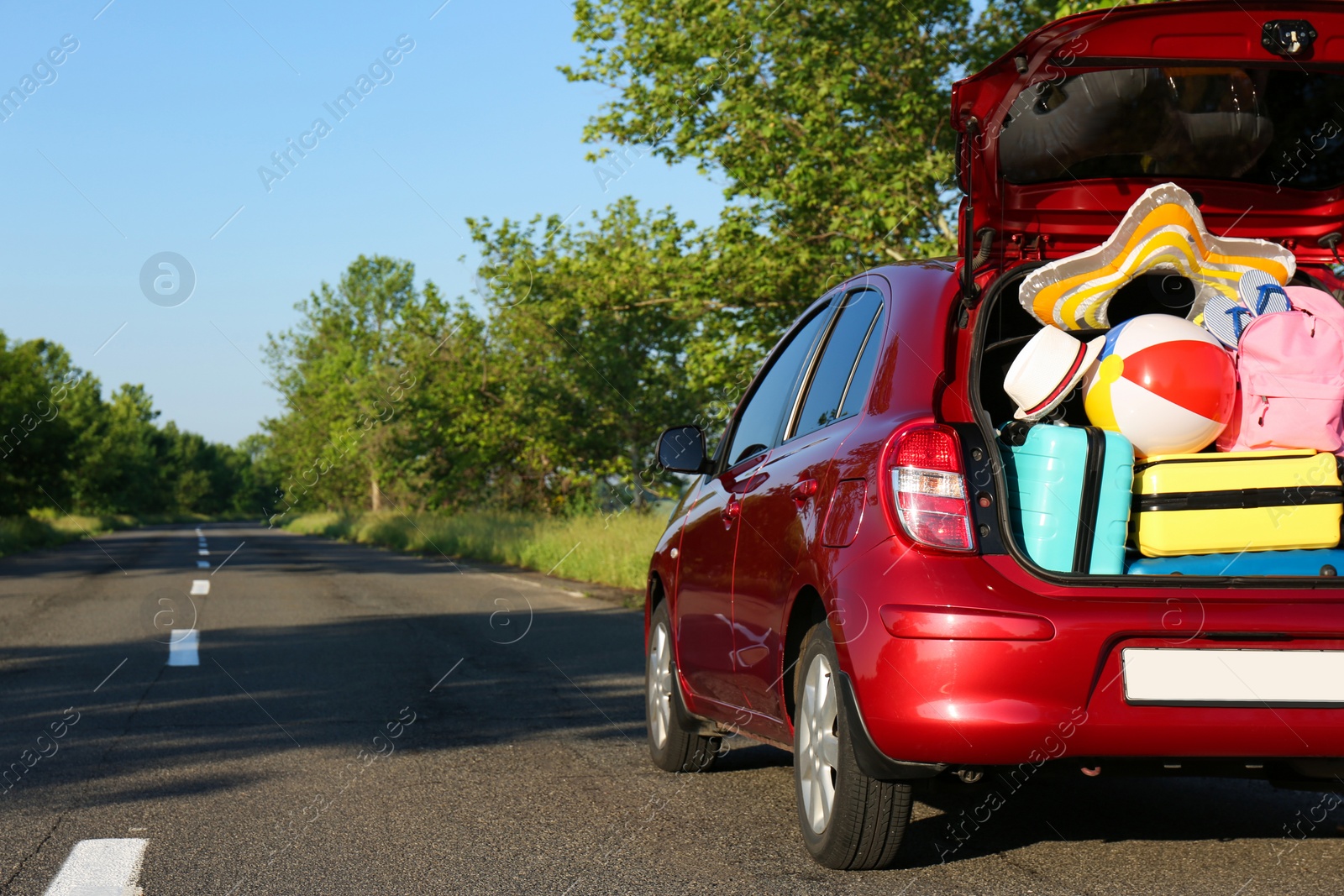 Photo of Family car with open trunk full of luggage on highway. Space for text