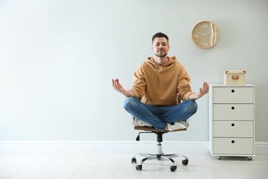 Photo of Calm man meditating in office chair at work. Space for text