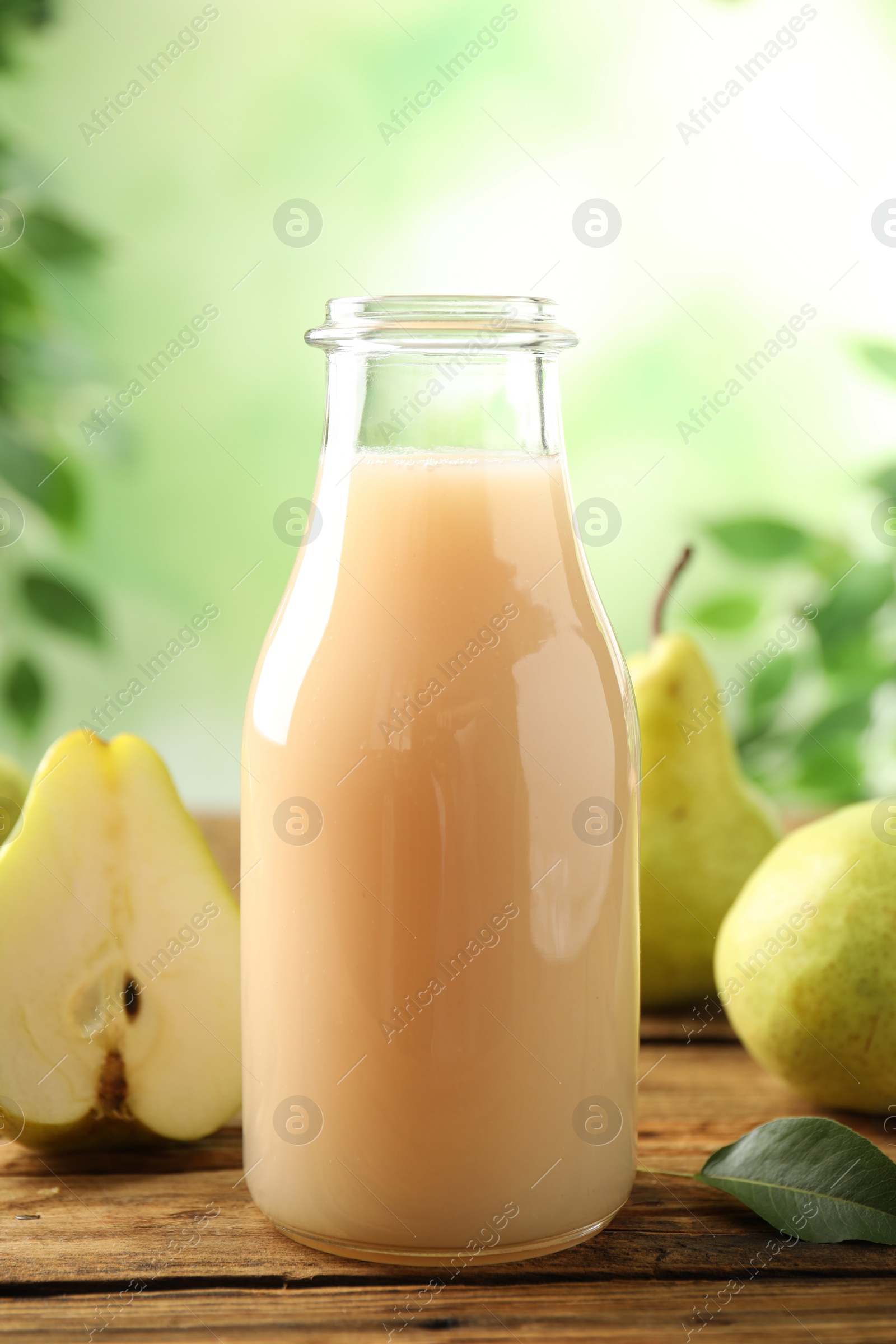 Photo of Fresh pear juice in glass bottle and fruits on wooden table, closeup