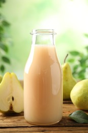 Photo of Fresh pear juice in glass bottle and fruits on wooden table, closeup