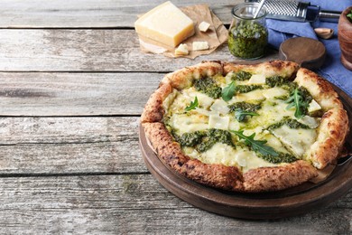 Photo of Delicious pizza with pesto, cheese and arugula on wooden table. Space for text