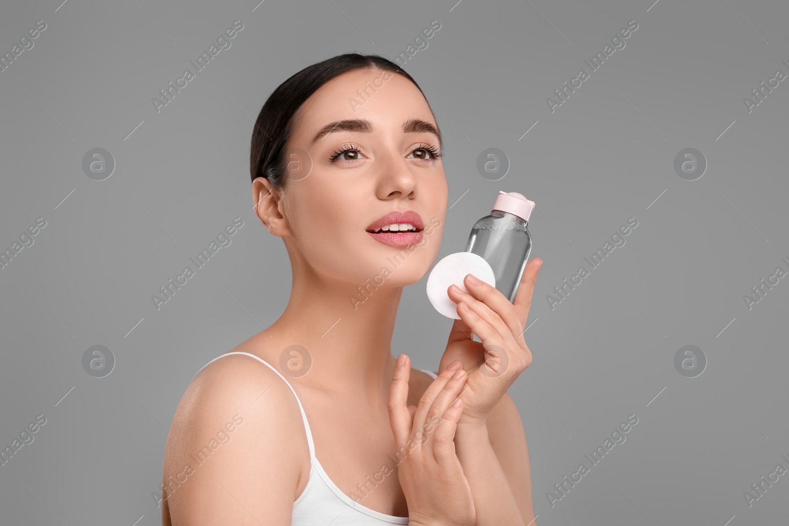 Photo of Beautiful woman with makeup remover and cotton pad on gray background