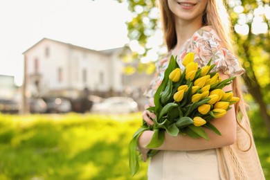 Photo of Teenage girl with bouquet of yellow tulips in city park on sunny day, closeup. Space for text