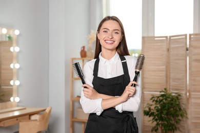 Photo of Portrait of happy hairdresser with brushes in beauty salon