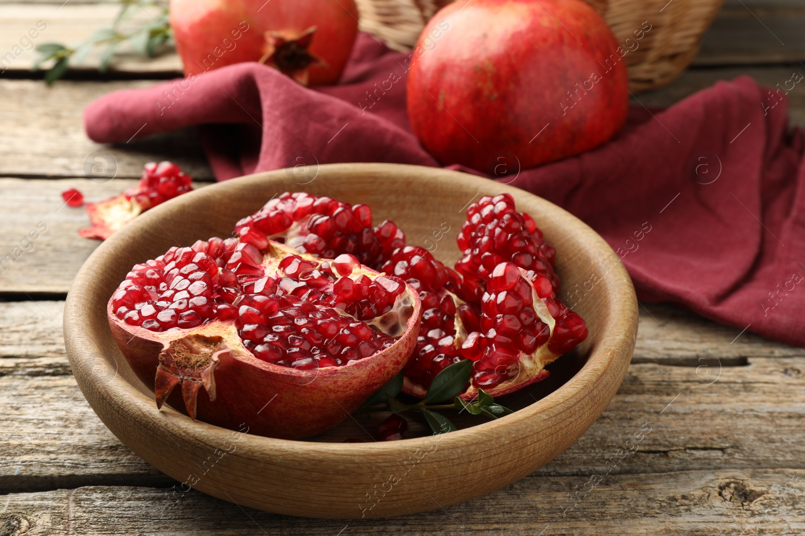 Photo of Fresh pomegranates and green leaves on wooden table, closeup