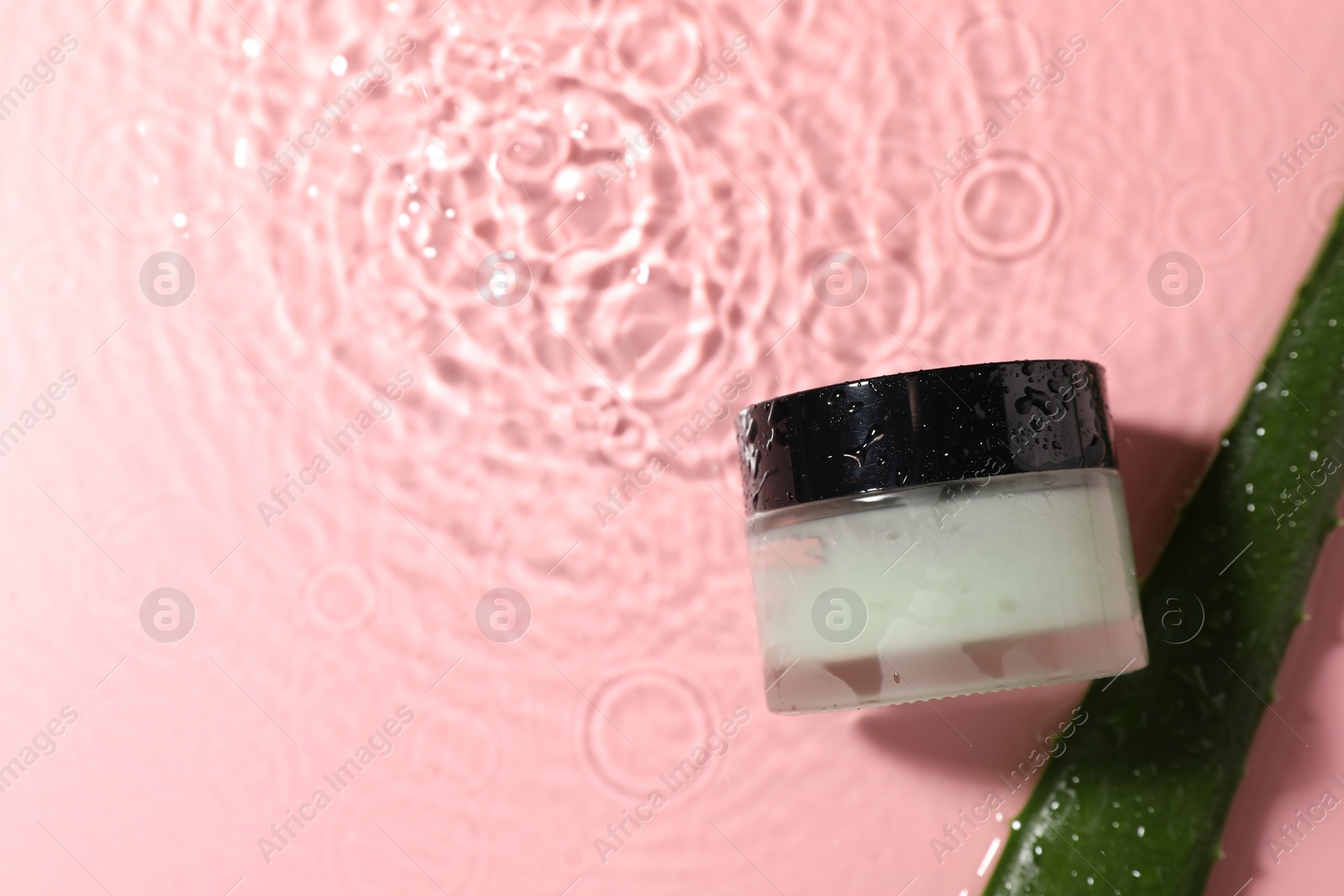 Photo of Jar of cosmetic product and aloe leaf in water on pink background, flat lay. Space for text