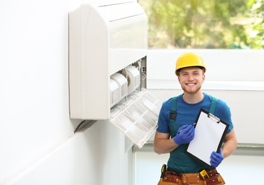 Professional technician with clipboard near modern air conditioner indoors