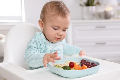 Photo of Cute little baby eating food in high chair at home