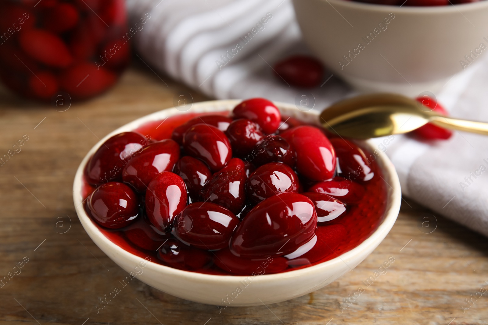 Photo of Delicious dogwood jam with berries in bowl on wooden table, closeup