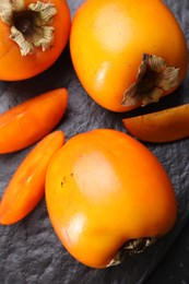 Photo of Delicious ripe persimmons on dark textured table, top view