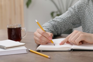 Woman writing in notebook at wooden table indoors, closeup