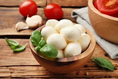 Photo of Delicious mozzarella balls and basil leaves in bowl on wooden table, closeup