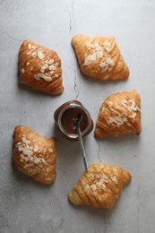 Delicious croissants with almond flakes and chocolate paste on grey table, flat lay