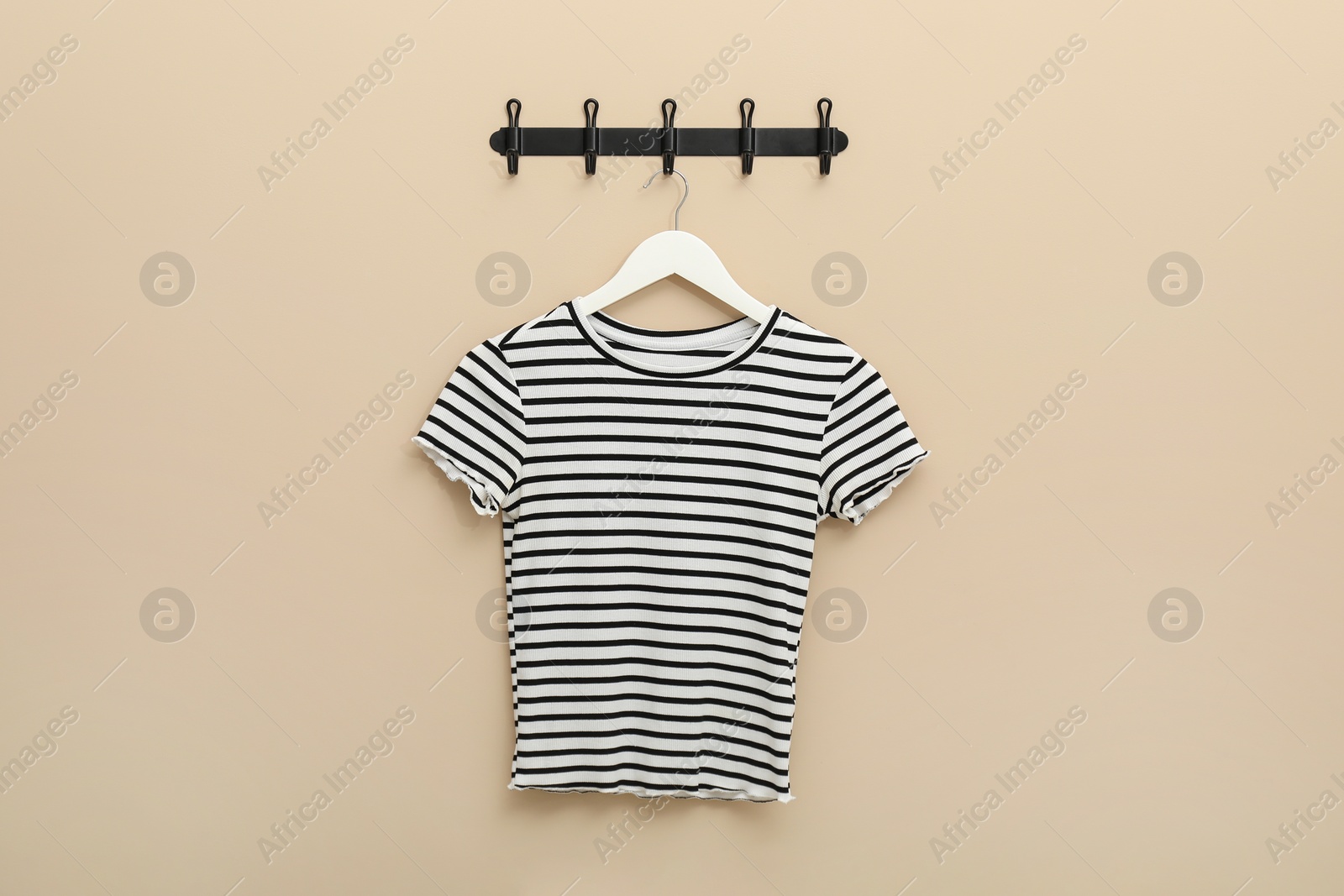 Photo of Hanger with striped t-shirt on beige wall