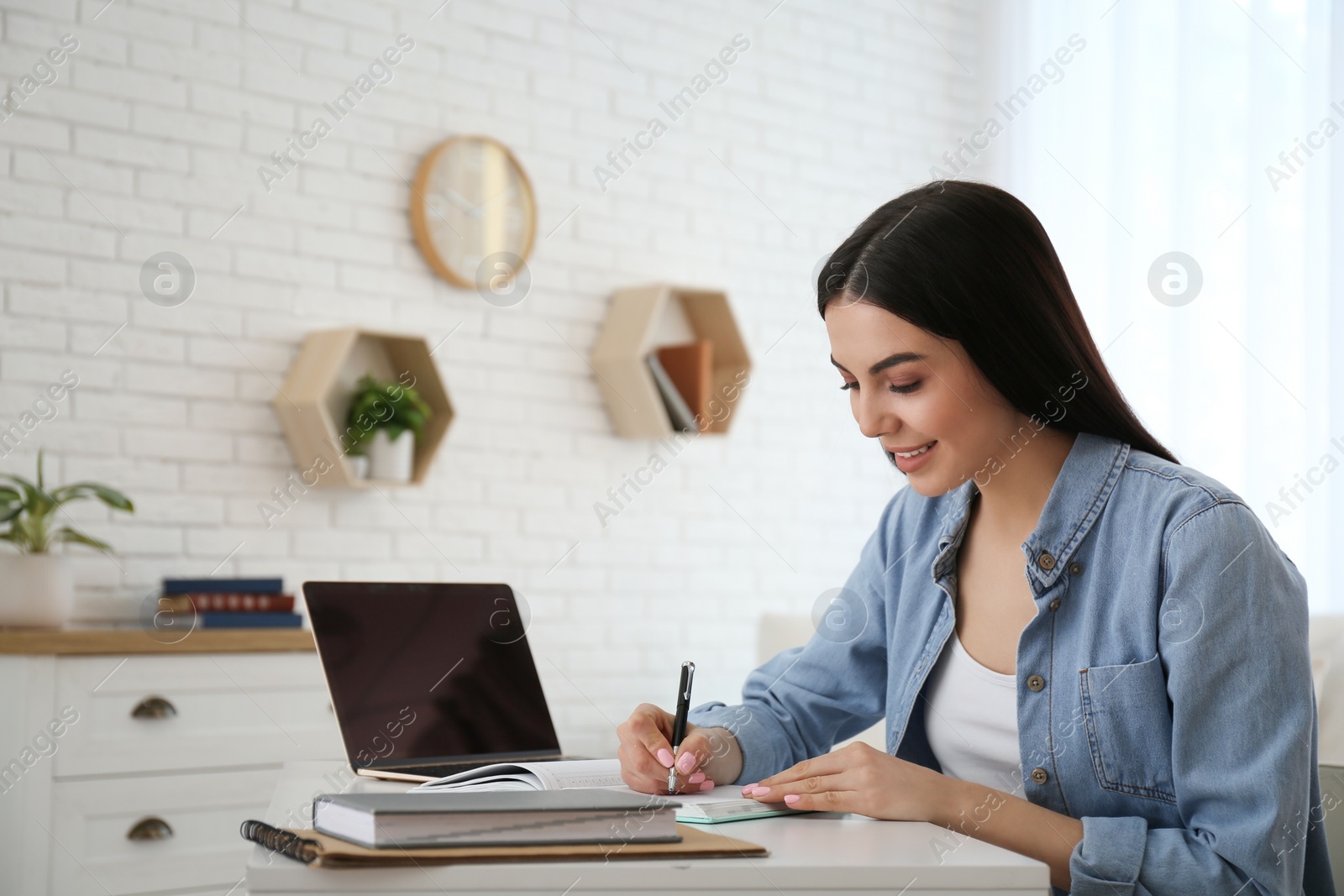 Photo of Young woman taking notes during online webinar at table indoors