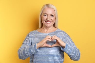Photo of Portrait of mature woman making heart with her hands on color background