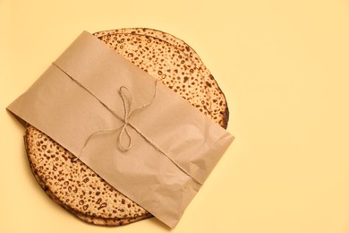 Photo of Top view of tasty matzos wrapped with paper on beige background, space for text. Passover (Pesach) celebration
